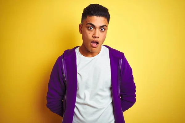 年轻的巴西男子穿着紫色运动衫站在孤立的黄色背景在震惊的脸 看起来怀疑和讽刺 惊讶与张开的嘴 — 图库照片