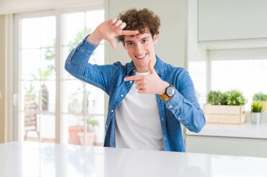 Evde rahat kot ceket giyen genç yakışıklı adam mutlu yüz ile elleri ve parmakları ile çerçeve yapma gülümseyerek. Yaratıcılık ve fotoğrafçılık konsepti.