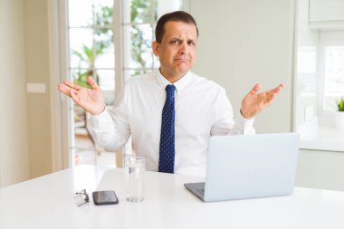 Orta yaş iş adamı bilgisayar dizüstü bilgisayar ile çalışan habersiz ve kolları ve elleri ile karışık ifade kaldırdı. Şüphe kavramı.