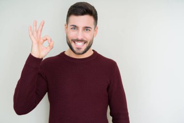 Genç yakışıklı adam izole arka plan üzerinde bir kazak giyen olumlu el ve parmakları ile ok işareti yapıyor gülümseyerek. Başarılı ifade.