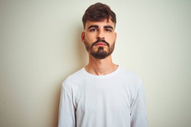 Dövme giyen genç adam izole beyaz arka plan üzerinde duran t-shirt yüzünde ciddi ifade ile rahat. Kameraya basit ve doğal bir bakış.
