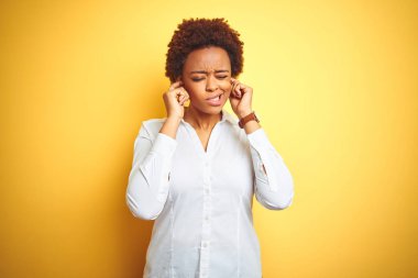Yüksek sesle müzik sesi için rahatsız ifade ile parmakları ile kulakları kapsayan izole sarı arka plan üzerinde Afro-Amerikan iş kadını. Sağır kavramı.