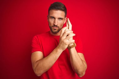 Genç yakışıklı adam kırmızı izole arka plan üzerinde rahat t-shirt giyen el hareketi ile sembolik silah holding, çekim silah öldürme oynarken, kızgın yüz