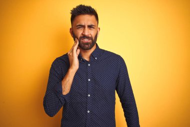 Genç yakışıklı Hintli işadamı izole sarı arka plan üzerinde diş ağrısı veya diş üzerinde diş hastalığı nedeniyle ağrılı ifade ile el ile ağız dokunmadan gömlek giyiyor. Diş hekimi konsepti.