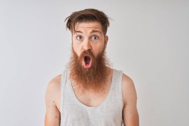 Genç kızıl İrlandalı adam izole gri arka plan üzerinde duran t-shirt giyen korkmuş ve sürpriz ifade, korku ve heyecanlı yüz ile şok.