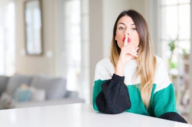 Evde kış kazak giyen genç güzel kadın dudaklarında parmak ile sessiz olmanı. Sessizlik ve gizli kavramı.