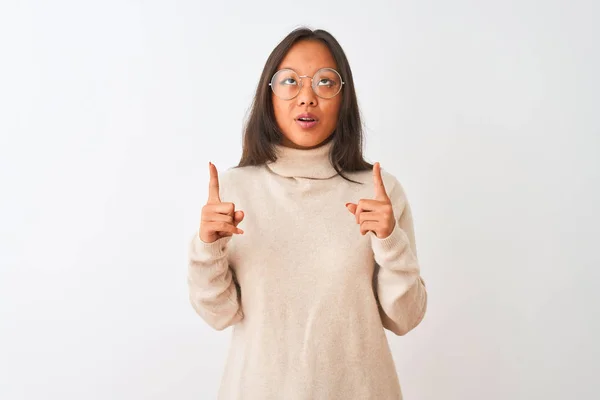 孤立した白い背景の上にタートルネックのセーターと眼鏡をかけた若い中国人女性は驚き 指で見上げて指を向け 腕を上げて驚いた — ストック写真