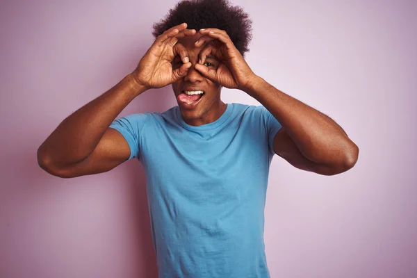 青いTシャツを着たアフリカ系アメリカ人男性は 孤立したピンクの背景の上に立って 舌を突き出し 指を通して目を見るようなOkジェスチャーをしています クレイジー表現 — ストック写真