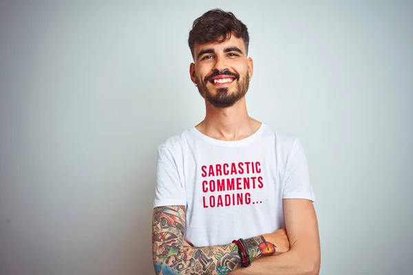Young man with tattoo wearing fanny t-shirt standing over isolated white background happy face smiling with crossed arms looking at the camera. Positive person.