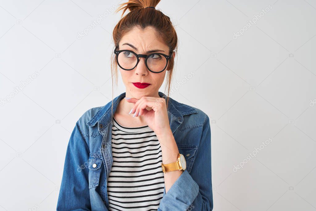 Redhead woman wearing denim shirt and glasses standing over isolated white background serious face thinking about question, very confused idea