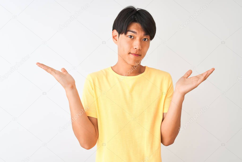 Chinese man wearing yellow casual t-shirt standing over isolated white background clueless and confused expression with arms and hands raised. Doubt concept.