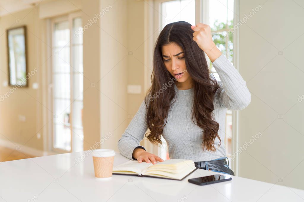 Young woman reading a book and drinking a coffe annoyed and frustrated shouting with anger, crazy and yelling with raised hand, anger concept