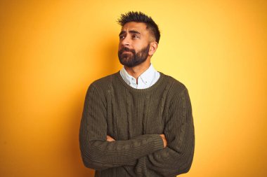 Yeşil kazak ve gömlek giyen genç hintli adam izole sarı arka plan üzerinde duran yan bakarak ve düşünme uzak bakıyor.