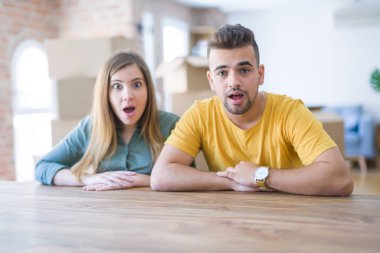 Genç çift arkalarında karton kutuları ile yeni eve movinto masada oturan korkmuş ve sürpriz ifade, korku ve heyecanlı yüz ile şok.