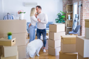 Karton kutular etrafında yeni evde ayakta köpek öpüşme ile genç güzel çift