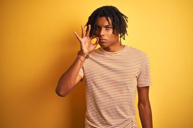 Izole sarı arka plan ağız ve dudaklar parmakları ile zip olarak kapalı üzerinde duran çizgili t-shirt giyen dreadlocks ile Afro adam. Gizli ve sessiz, tabu konuşma