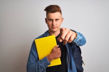Denim gömlek sırt çantası dizüstü bilgisayar giyen genç öğrenci adam kamera ve size parmak ile işaret izole beyaz arka plan üzerinde, el işareti, önden olumlu ve kendinden emin jest