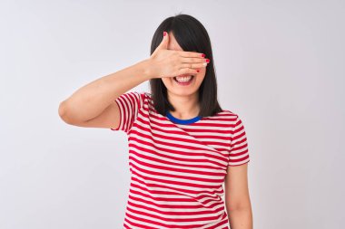 Genç güzel Çinli kadın izole beyaz arka plan üzerinde kırmızı çizgili t-shirt giyen gülümseyerek ve sürpriz için gözleri kaplayan yüz el ile gülüyor. Kör kavramı.