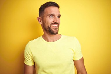 Genç yakışıklı adam sarı izole arka plan üzerinde rahat sarı t-shirt giyen yüzünde gülümseme, doğal ifade ile yan bakıyor. Gülmekten emin.
