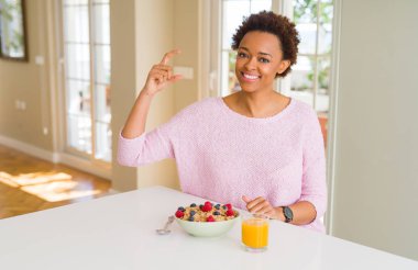Sabahları evde sağlıklı kahvaltı yapan genç afro-amerikalı kadın gülümseyerek ve kendinden emin bir şekilde el iyle el leriyle işaret yaparken parmaklarla ve kameraya bakıyor. Ölçü kavramı.