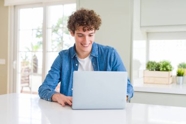 Mutlu bir yüz ayakta ve dişleri gösteren kendinden emin bir gülümseme ile gülümseyen bilgisayar dizüstü bilgisayar kullanan genç adam