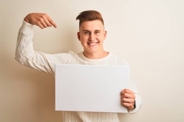 Genç yakışıklı adam kendini işaret sürpriz yüzü ile izole beyaz arka plan üzerinde duran afiş tutan