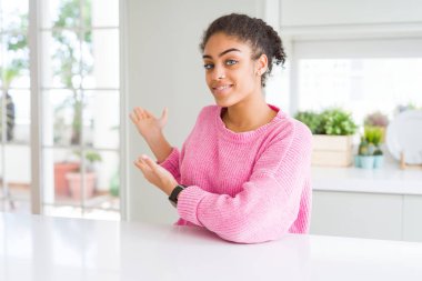 Afro saçlı güzel afro-amerikan kadın rahat pembe kazak giyen açık el ile doğal gülümseyen girmek için davet