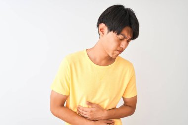 Sarı rahat t-shirt giyen Çinli adam mide üzerinde el ile izole beyaz arka plan üzerinde duran çünkü mide bulantısı, ağrılı hastalık kötü hissediyorum. Ağrı kavramı.