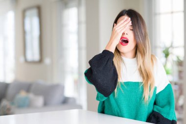 Evde kış kazak giyen genç güzel kadın yarım yüz, göz ve ağız el ile kapsayan Yawning yorgun. Acı yüzü acıyor.