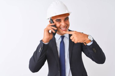 İzole beyaz arka plan üzerinde akıllı telefonda konuşurken kask giyen genç mimar adam çok mutlu el ve parmak ile işaret