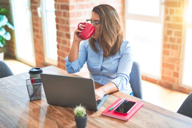 Genç iş kadını bilgisayar dizüstü bilgisayar kullanarak çalışan masada oturan, ofiste bir fincan kahve içme