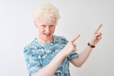 Genç albino sarışın adam izole beyaz arka plan üzerinde duran rahat t-shirt giyen gülümseyerek ve yan iki el ve parmakları ile işaret kamera bakıyor.