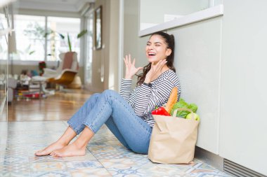 Mutfak zemininde oturan genç kadın taze bakkaliye dolu bir poşetle delice ve çılgın bir şekilde başarı için kolları kaldırıp, gözleri kapalı çığlık atarak heyecanla bağırıyor. Kazanan kavramı