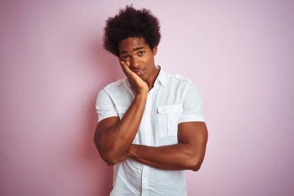 Young american man with afro hair wearing white shirt standing over isolated pink background thinking looking tired and bored with depression problems with crossed arms.