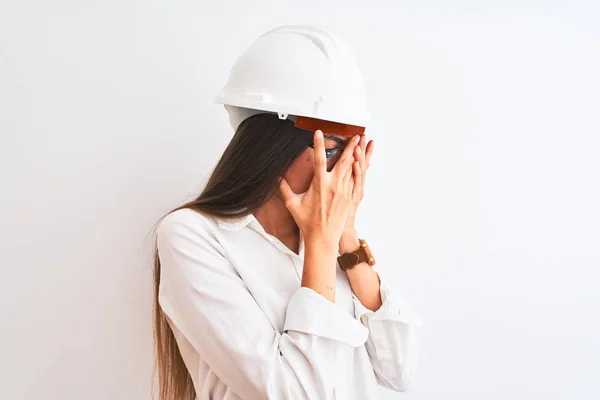 年轻的美丽的建筑师妇女戴着头盔和眼镜在孤立的白色背景与悲伤的表情覆盖脸与双手 而哭泣 抑郁症概念 — 图库照片