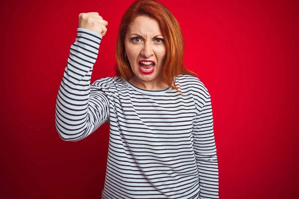 年轻的红发妇女穿着带肩带海军衬衫站在红色孤立的背景愤怒和疯狂的举起拳头沮丧和愤怒 而愤怒地喊道 愤怒和侵略性的概念 — 图库照片