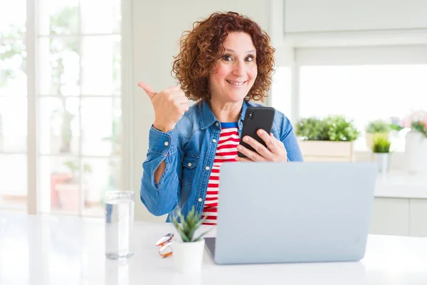 高级妇女使用笔记本电脑和智能手机指向和显示与大拇指到一边与快乐的脸微笑 — 图库照片