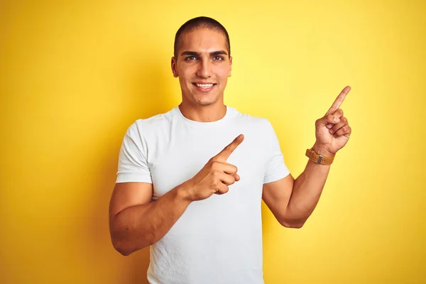 年轻的白人男子穿着休闲的白色T恤在黄色孤立的背景微笑 看着相机指着两只手和手指的一侧 — 图库照片
