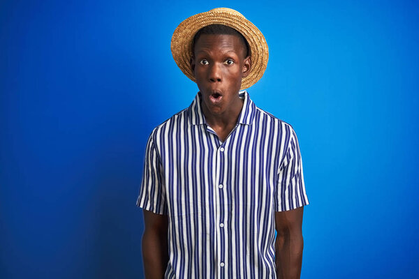 African american man wearing striped shirt and summer hat over isolated blue background afraid and shocked with surprise expression, fear and excited face.