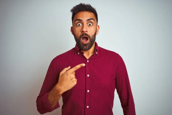 年轻的印度男子穿着红色优雅的衬衫站在孤立的灰色背景惊讶用手指指着一边 张开嘴惊讶的表情 — 图库照片