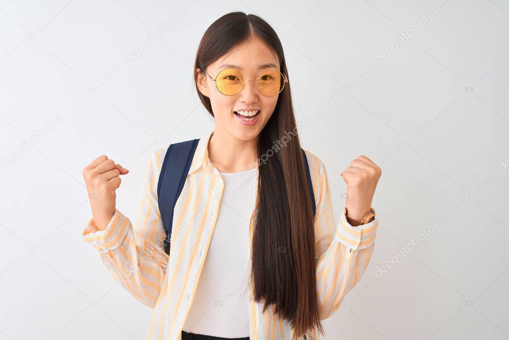 Young chinese student woman wearing glasses and backpack over isolated white background celebrating surprised and amazed for success with arms raised and open eyes. Winner concept.