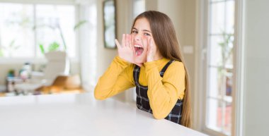 Güzel genç kız çocuk masada bağırarak oturan ve ağız da el ile yan yüksek sesle bağırıyor. İletişim kavramı.