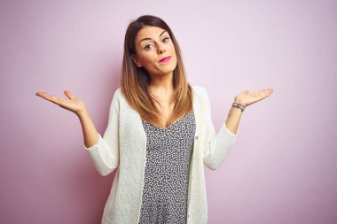 Genç güzel kadın pembe izole arka plan üzerinde duran habersiz ve kolları ve elleri ile karışık ifade kaldırdı. Şüphe kavramı.