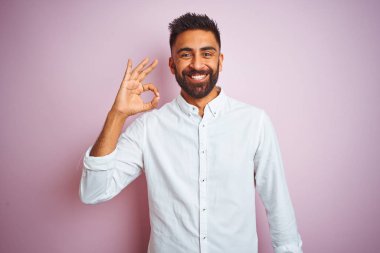 Genç Hintli işadamı izole pembe arka plan üzerinde duran zarif gömlek giyen el ve parmakları ile ok işareti yapıyor olumlu gülümseyerek. Başarılı ifade.