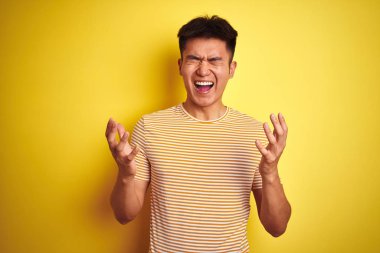 Genç Asyalı Çinli adam izole sarı arka plan üzerinde duran t-shirt giyen silah kaldırdı ve kapalı gözleri heyecan çığlık ile başarı için deli ve deli kutluyor. Kazanan kavramı