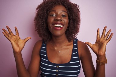 Genç Afrikalı afro kadın çizgili t-shirt giyen izole pembe arka plan üzerinde duran deli kutluyor ve kollarını kaldırdı ve açık gözleri heyecan çığlık ile başarı için hayran. Kazanan kavramı