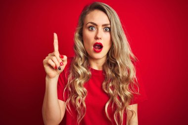 Genç güzel kadın başarılı bir fikir ile parmak işaret kırmızı izole arka plan üzerinde duran temel t-shirt giyiyor. Çıktı ve mutlu. Bir numara.