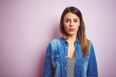 Genç güzel kadın yüzünde ciddi bir ifade ile pembe izole arka plan üzerinde duran. Kameraya basit ve doğal bir bakış.