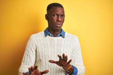 Izole sarı arka plan üzerinde denim gömlek ve beyaz kazak giyen Afro-Amerikan adam korku ve ifade ile reddetme ve inkar gösteren avuç içi uzak hareketli. Dur ve yasak.