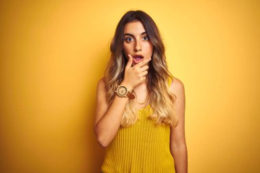 Genç güzel kadın sarı izole arka plan üzerinde t-shirt giyen güvensizlik, sürpriz ve çene elleri ile hayran ifade hayran arıyorum